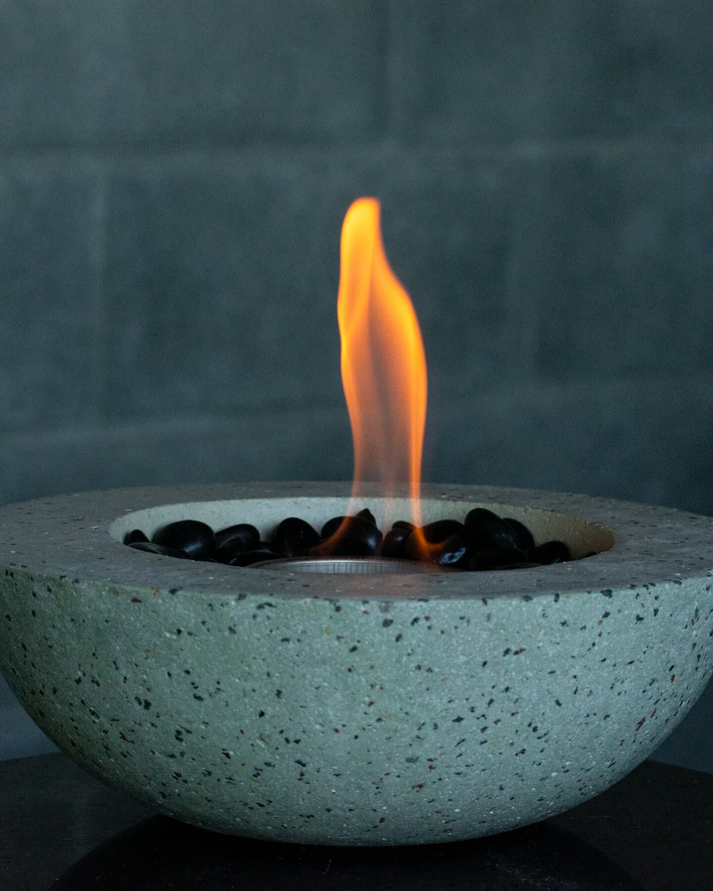 Boreal: fuego de mesa de concreto verde grisáceo con piedras negras y la llama encendida