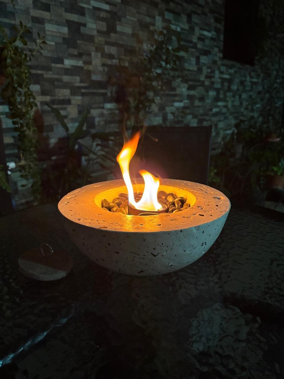 Ámbaris: fuego de mesa de concreto con fragmentos de vidrio ámbar, encendido de noche en una terraza