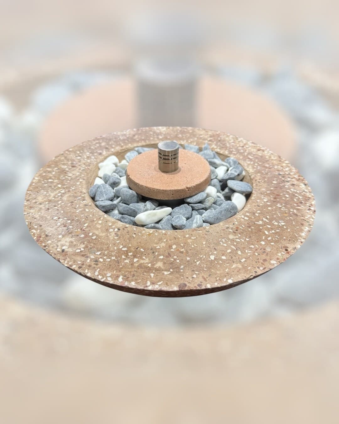 Arcadia: fuego de mesa de concreto en tonos terracota con acabado tipo terrazo, con piedras grises y blancas alrededor del quemador